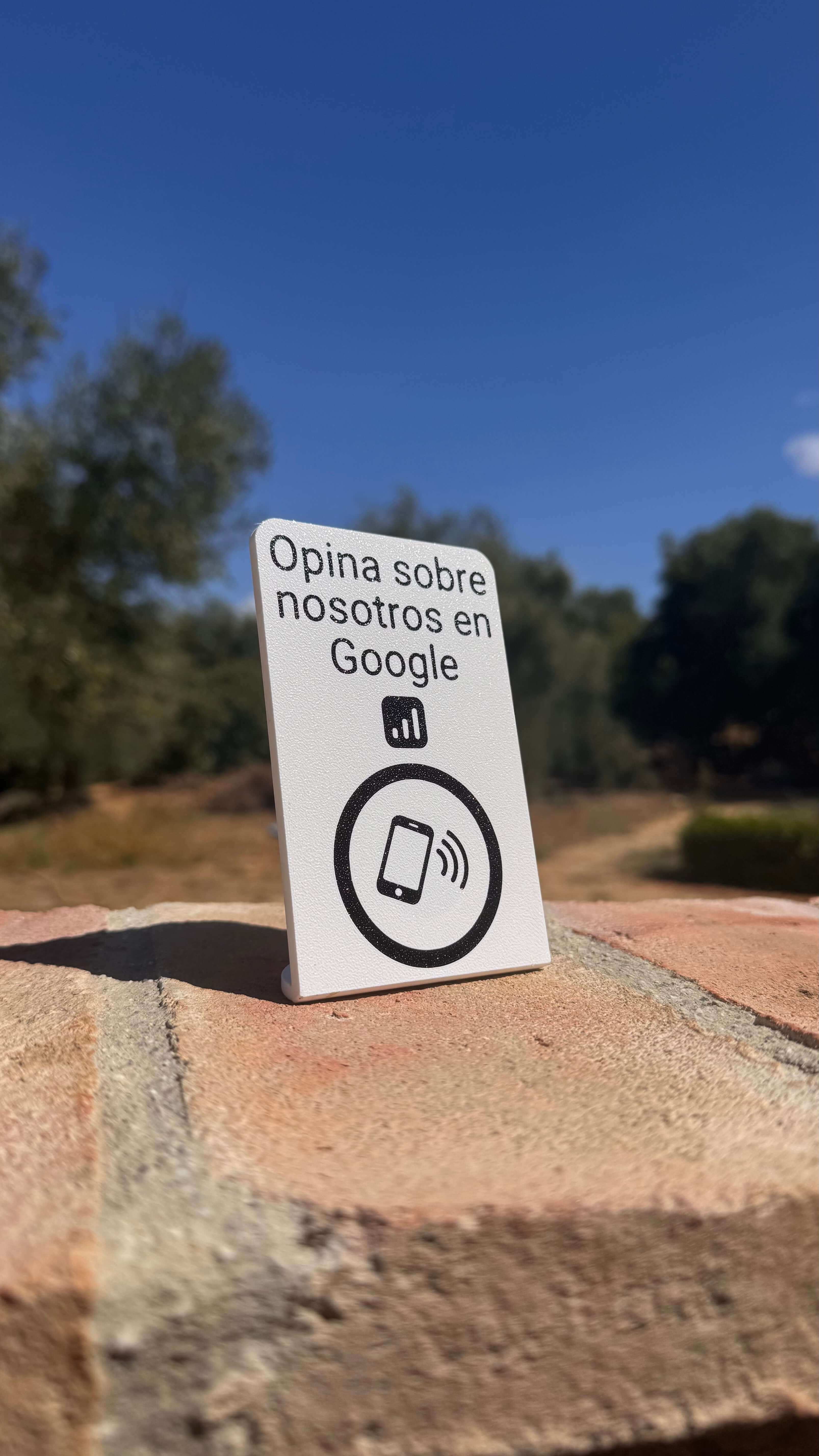 Stand NFC para reseñas en Google apoyado sobre un muro de piedra al aire libre, vista frontal