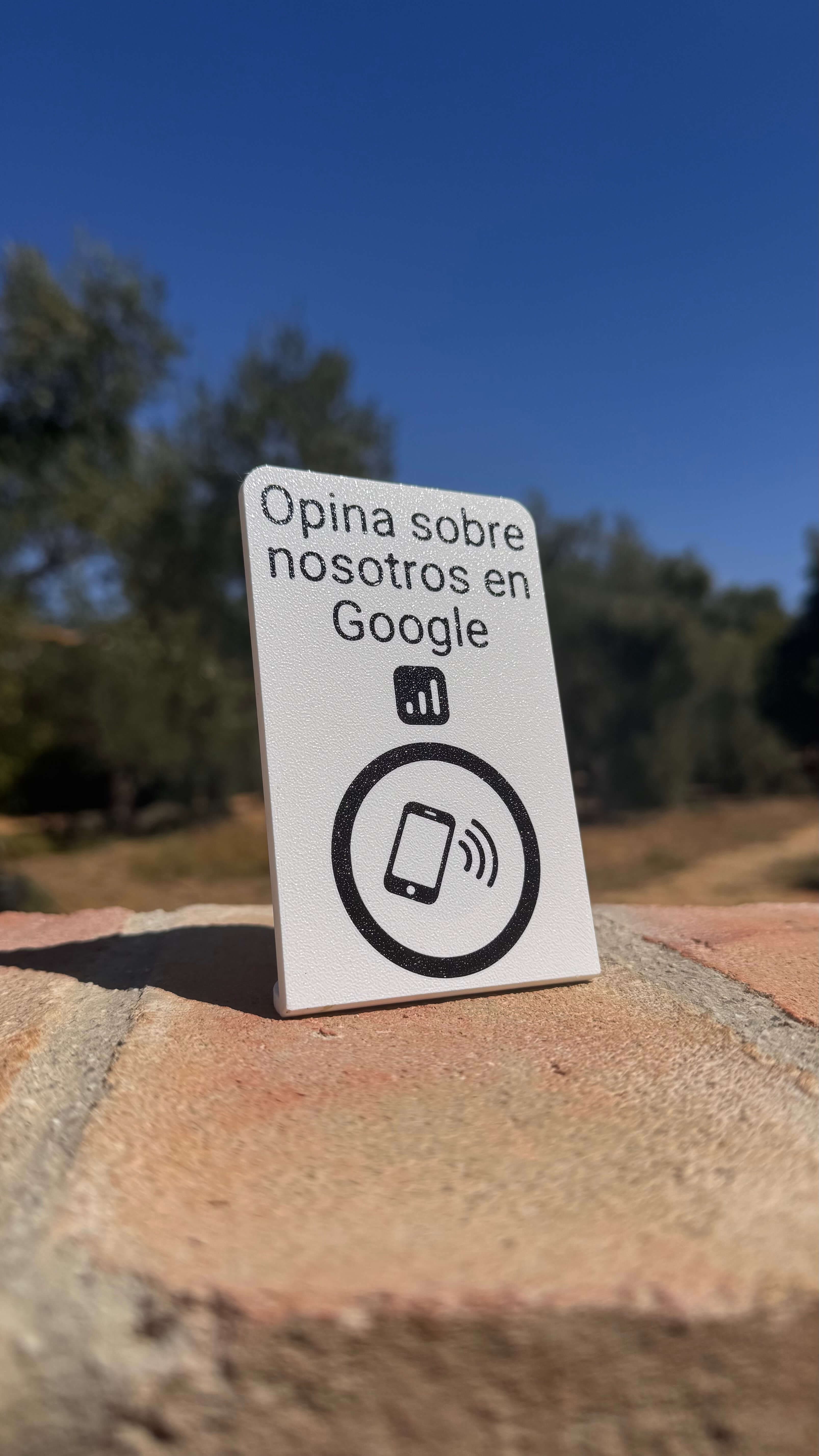 Stand NFC para reseñas en Google apoyado sobre un muro de piedra al aire libre, vista de perfil