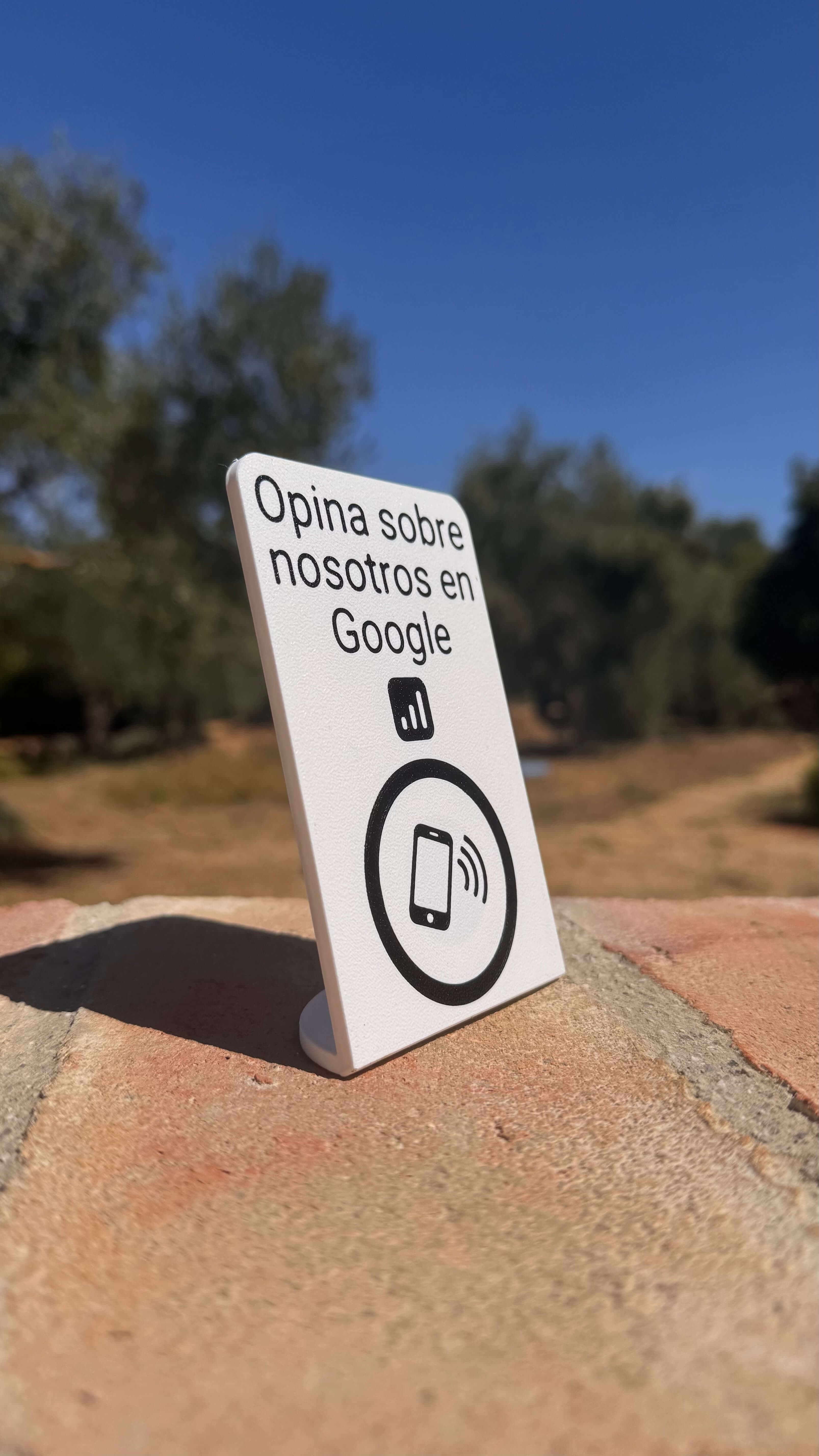Stand NFC para reseñas en Google apoyado sobre un muro de piedra al aire libre, en ángulo