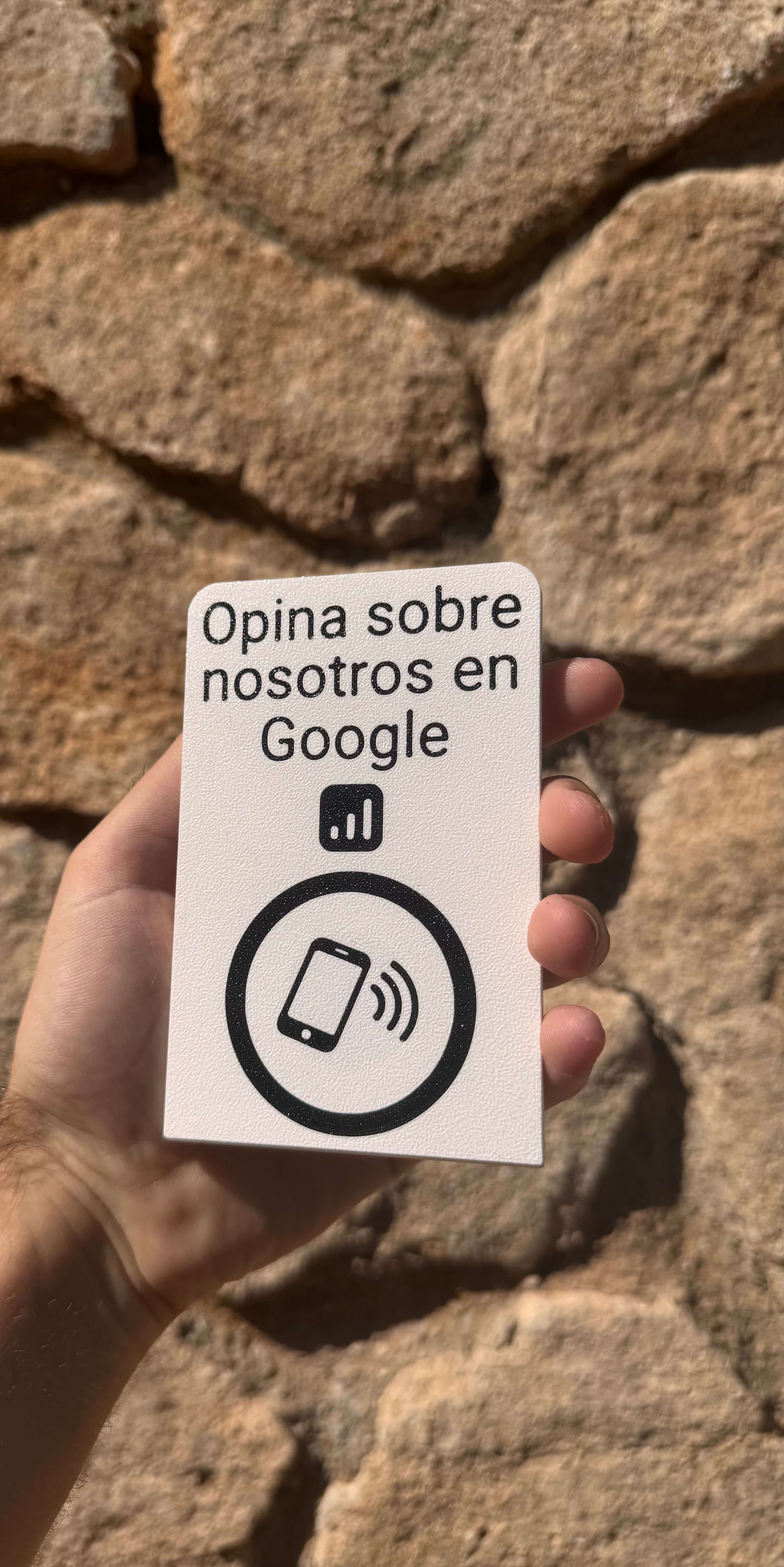 Stand NFC para reseñas en Google sujetado con la mano junto a un muro de piedra